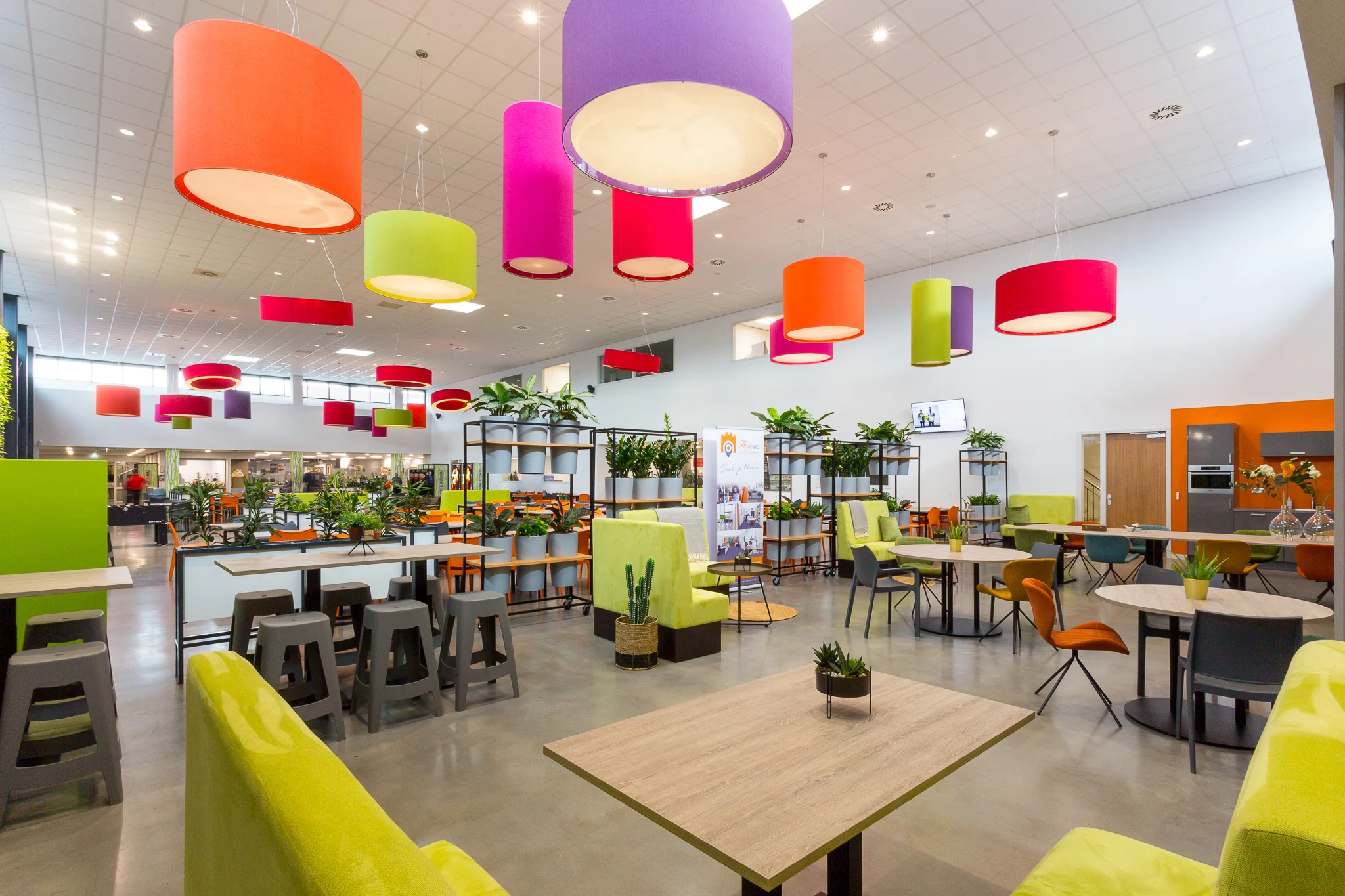 Moderne en kleurrijke kantineruimte aan de Niels Bohrweg met felgekleurde lampen, planten en diverse zitgelegenheden.